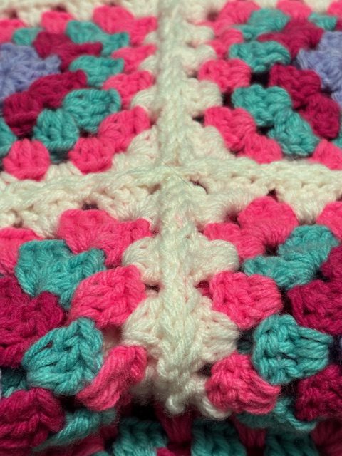 Close-up of a crochet blanket featuring a vibrant pattern of pink, teal, and cream-colored yarn.