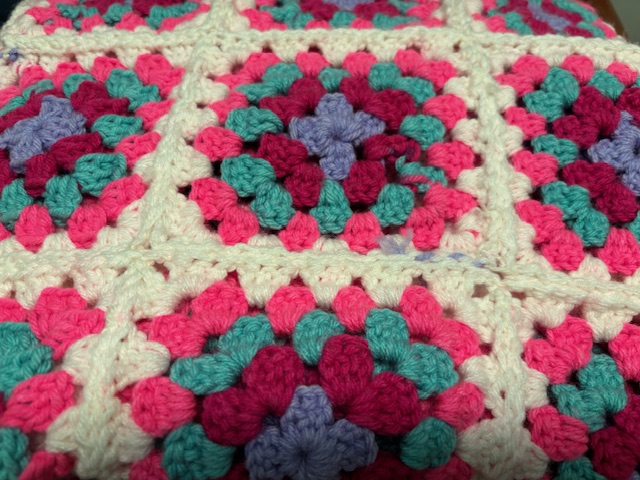 Close-up of a colorful crocheted square featuring a floral design in pink, turquoise, purple, and cream yarn.