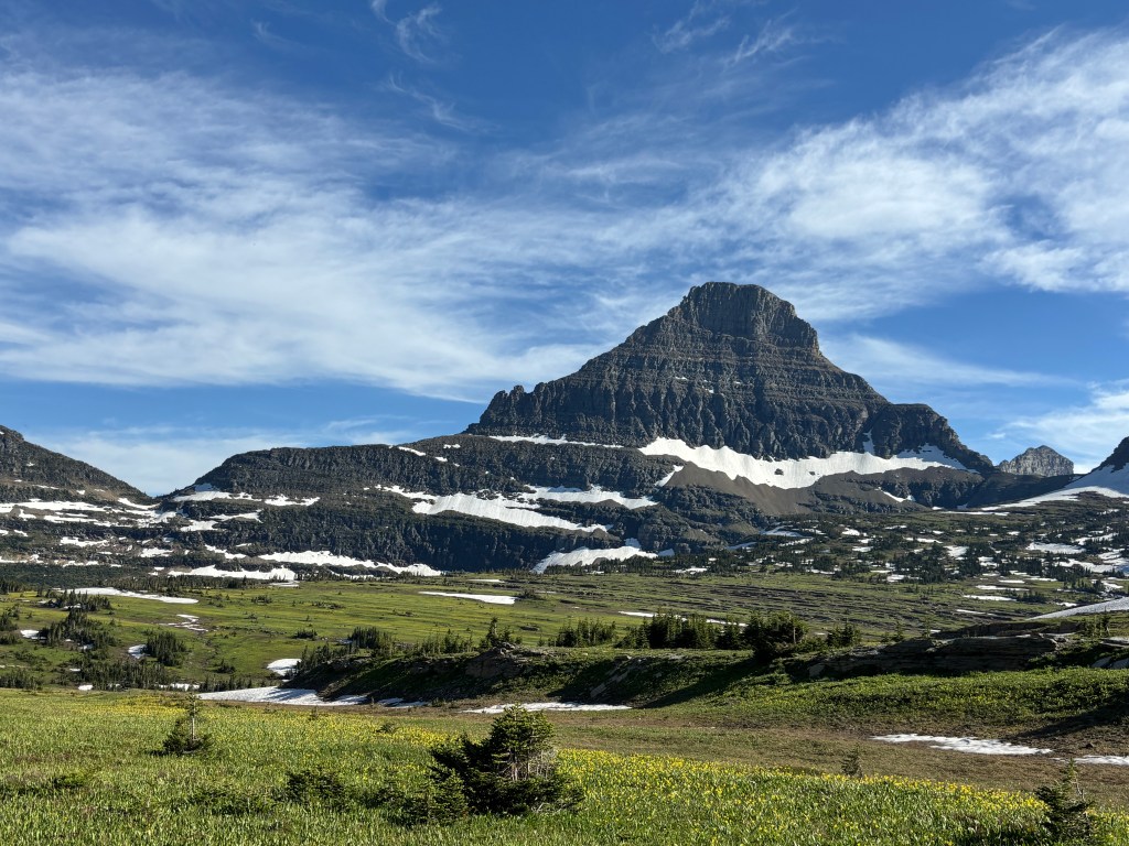 A scenic view of a mountainous landscape with patches of snow and lush green meadows under a clear blue sky.