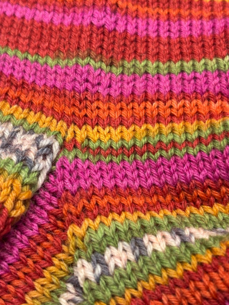 Close-up of vibrantly colored knitted fabric featuring stripes in pink, orange, green, and red tones.