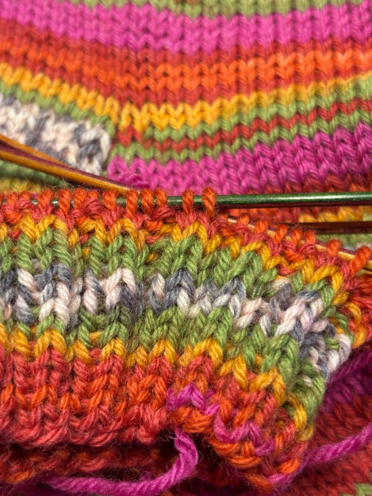Close-up of vibrant, multicolored yarn textures in a knitting project with a focus on stitches.