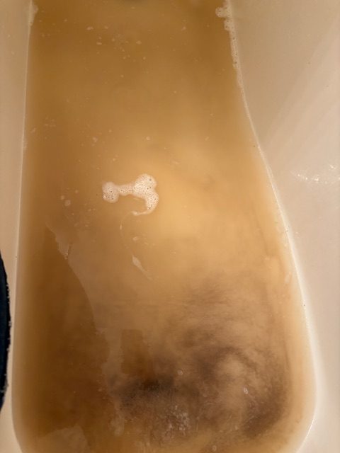 Dirty water in a bathtub after washing fleece, showing brownish color and foam.