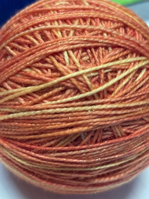 A close-up image of a ball of orange and cream yarn, showing the intricate layers and textures.