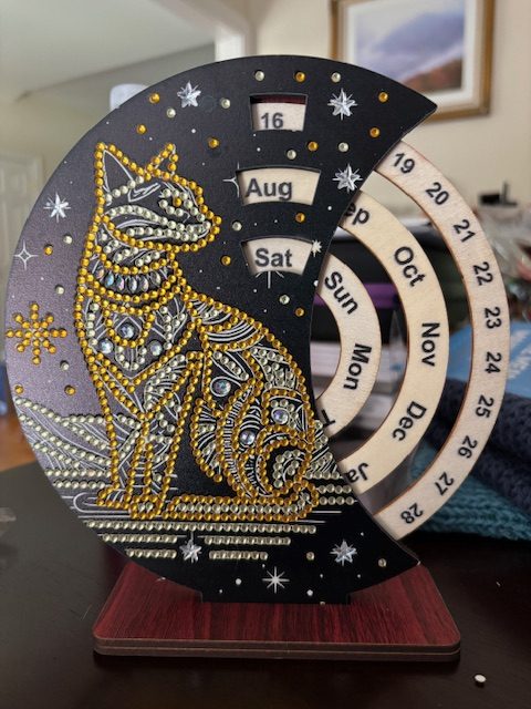 A decorative perpetual calendar featuring a cat design embellished with rhinestones, displaying days and months.