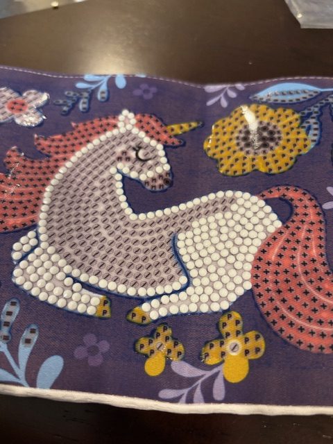 Close-up of a diamond painting project featuring a unicorn design with colorful rhinestones on a dark purple background.