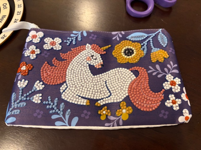 A colorful zipper pouch featuring a unicorn design made with rhinestones, surrounded by floral patterns.