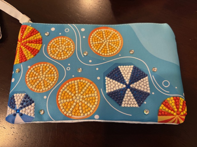 A colorful diamond painting zipper pouch featuring vibrant patterns of citrus slices and umbrellas on a blue background.