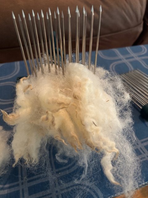 A close-up of wool combs loaded with fleece, showcasing the sharp metal tines and fluffy fibers, ready for processing.