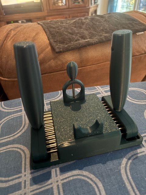 A set of wool combs placed on a blue patterned tablecloth, with a brown sofa in the background.