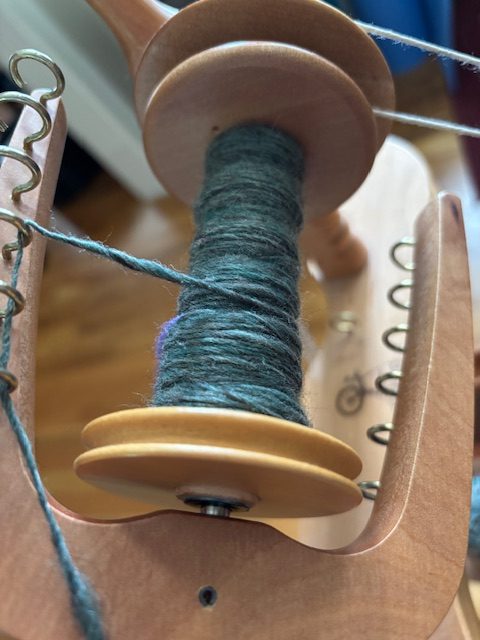 Close-up view of a spinning wheel bobbin with green wool yarn being spun.