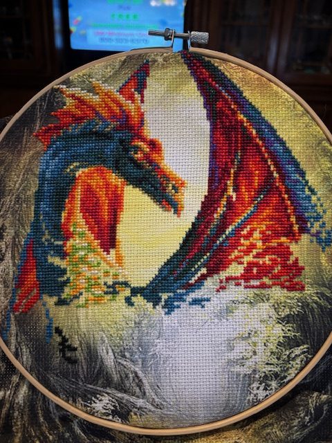 Close-up of a dragon cross stitch in progress, featuring vibrant colors and intricate stitching details.