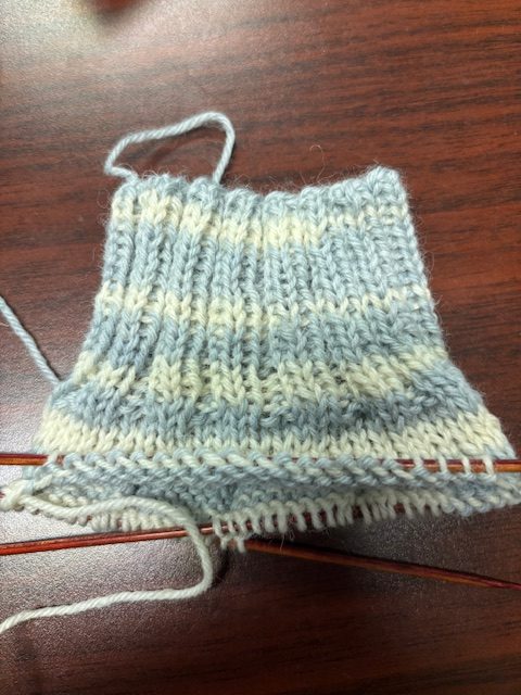 A partially knitted sock in a blue and cream striped pattern, resting on a wooden table.