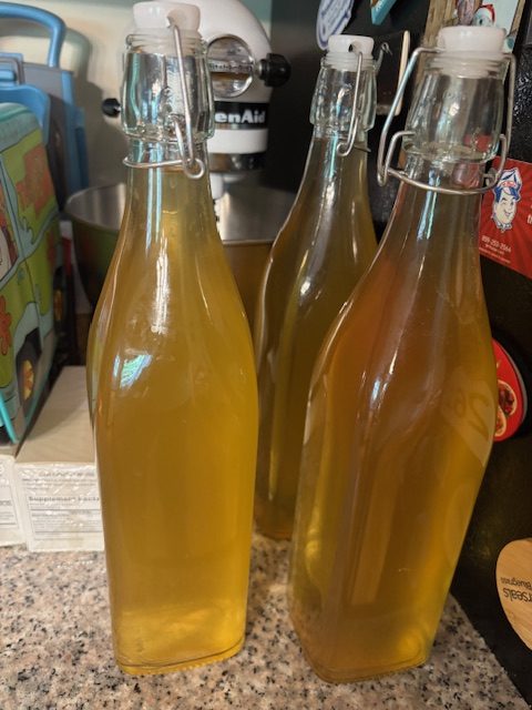 Three bottles of homemade mead with a yellowish liquid, placed on a kitchen countertop.