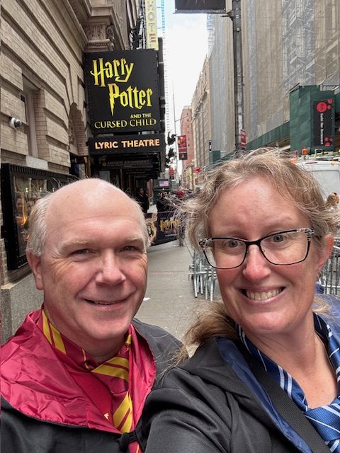 A selfie of two people wearing Harry Potter robes in front of the Lyric Theatre, which is advertising the show 'Harry Potter and the Cursed Child'.