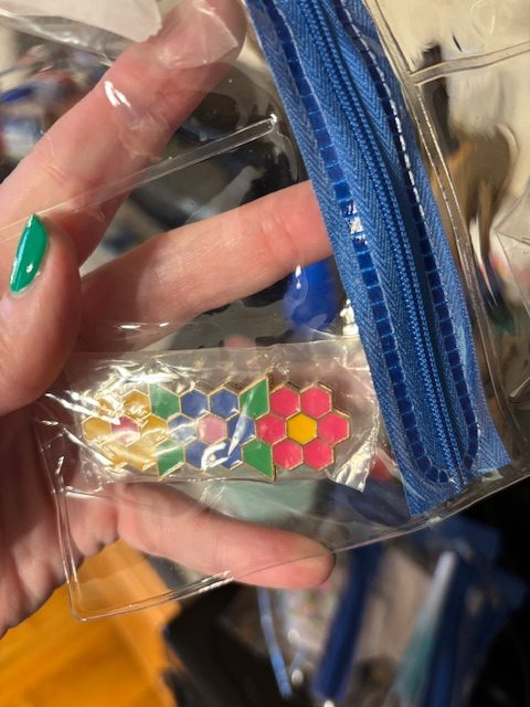A hand holding a clear plastic pouch containing colorful hexagon-shaped pieces in various colors including pink, green, yellow, and blue.