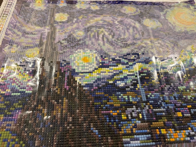 Close-up of a diamond painting kit depicting a starry night scene, featuring colorful rhinestones on a canvas with swirls and stars.