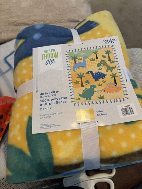 A folded no-sew throw kit featuring a dinosaur design, made of 100% polyester anti-pill fleece, measuring 48 inches by 60 inches, priced at $24.99.