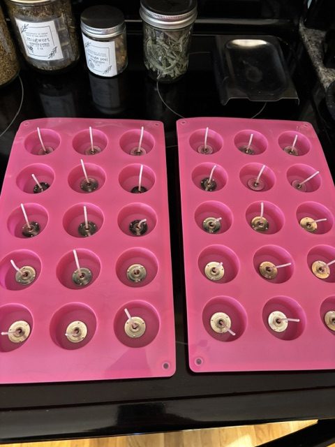 Two silicone candle molds filled with wicks, set on a stove. The molds are pink and feature multiple cavities for pouring wax.