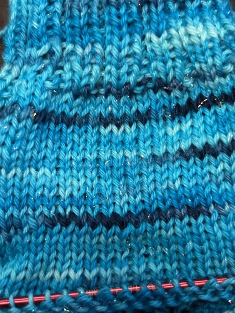 Close-up of knitted fabric in various shades of blue, featuring a striped pattern with some sparkle.