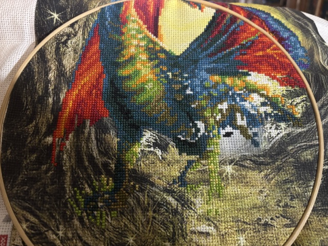 Close-up of a colorful cross-stitch embroidery featuring a mythical creature surrounded by foliage.